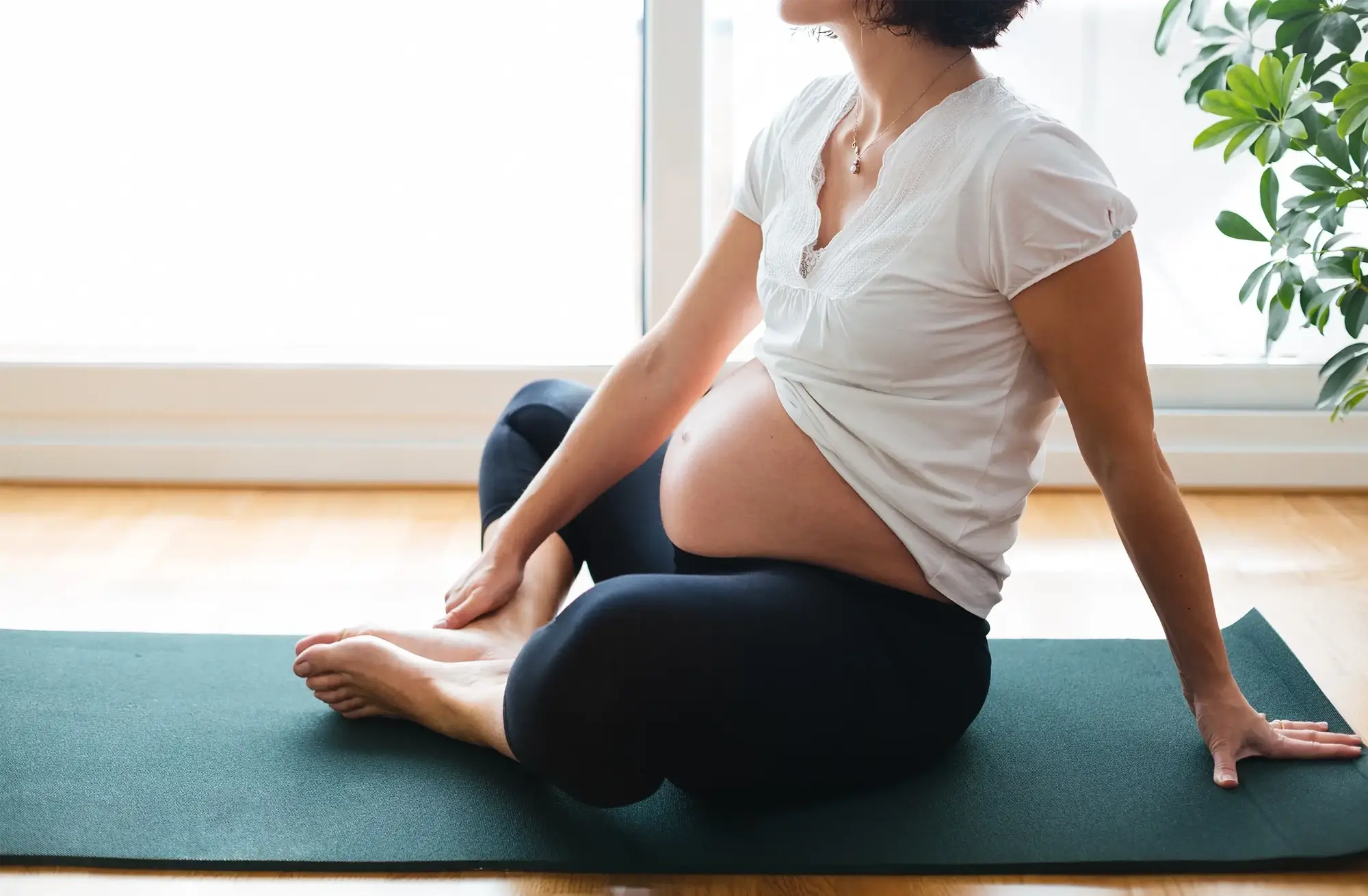 Expectant parent in a white dress holding their belly and smiling.