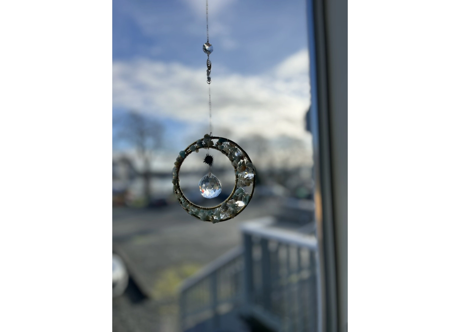 Crystal sun catcher shaped like a crescent with a hanging prism, photographed in a window with an outdoor background.