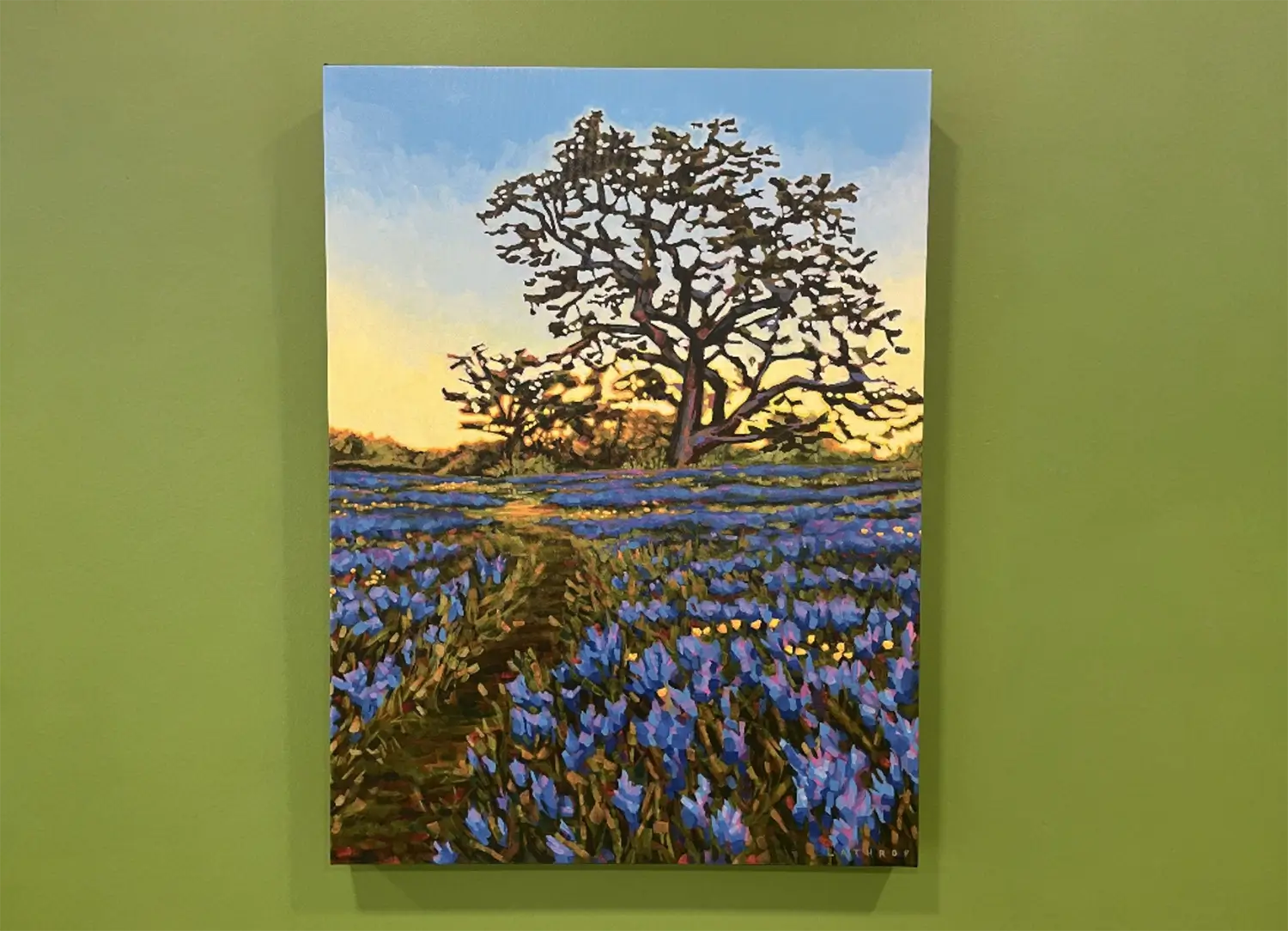 Colorful landscape painting of a large silhouetted tree at sunset, overlooking a field of blue wildflowers with a narrow path leading into the distance.