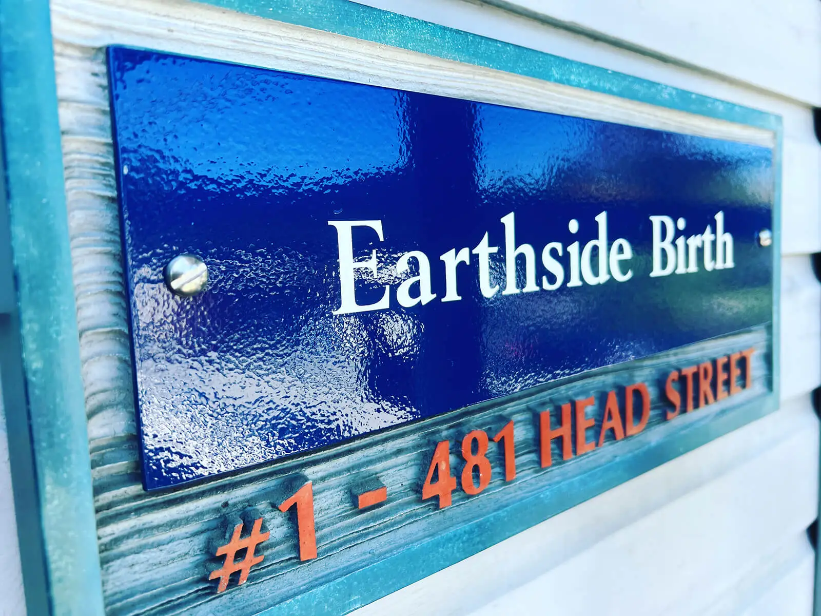 Close-up of the Earthside Birth clinic sign mounted on an exterior wall, showing the business name and street number.