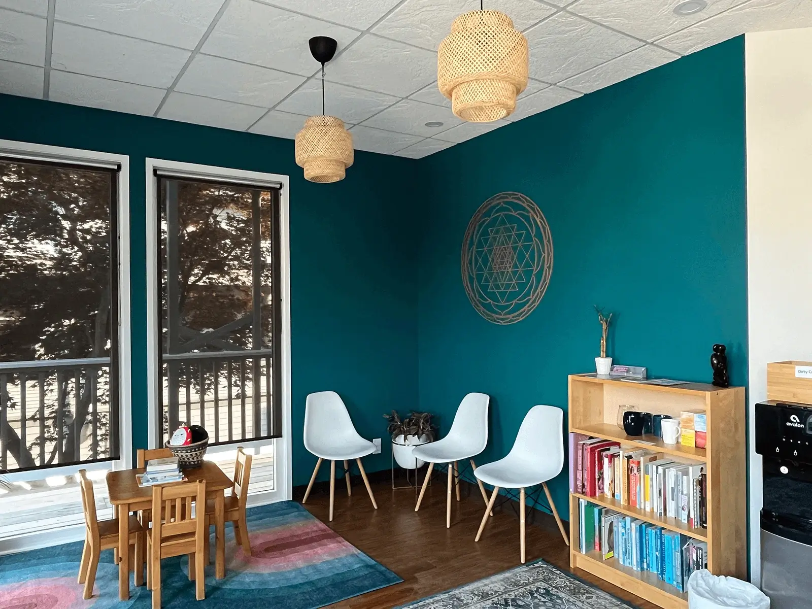 Bright and welcoming clinic waiting room with teal accent wall, white chairs, children's table, bookshelves, and natural woven light fixtures.